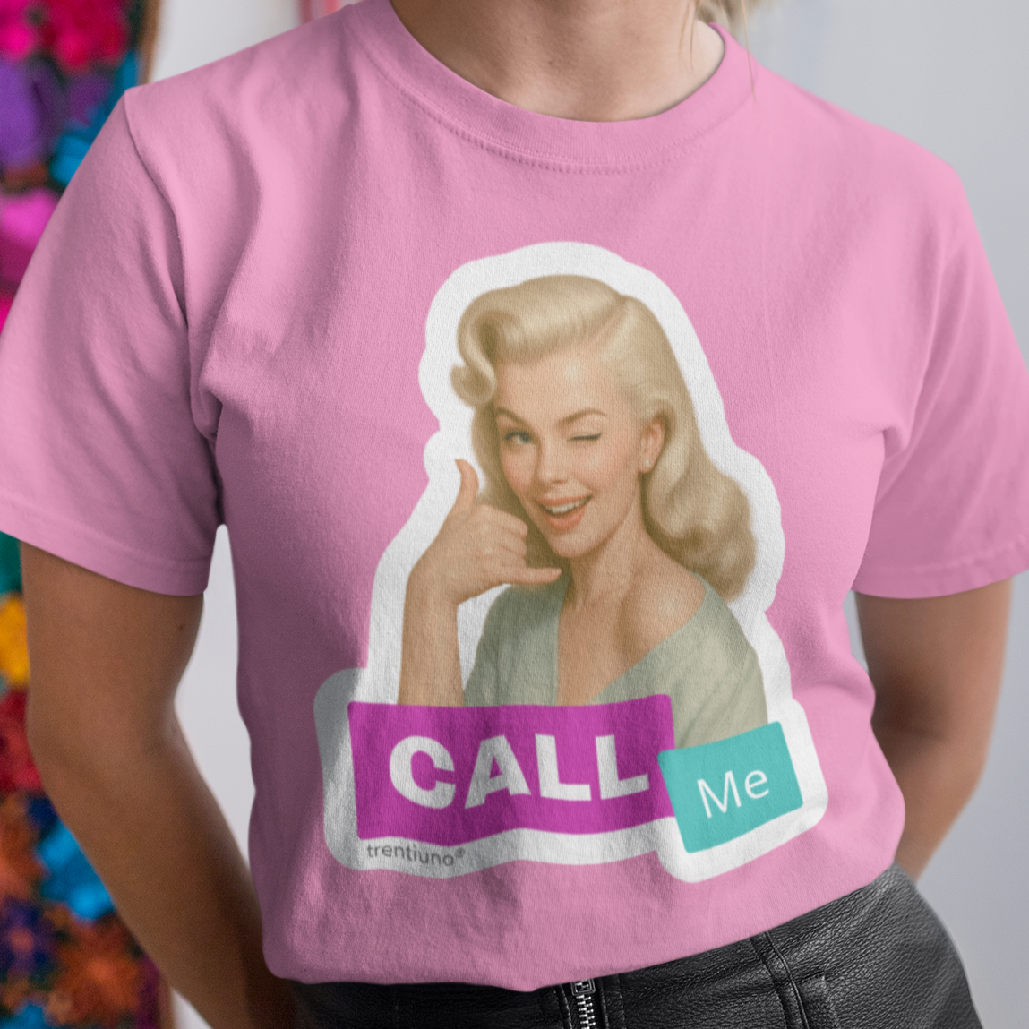 Person wearing a pink t-shirt with a graphic design and text, standing against a colorful floral wall.